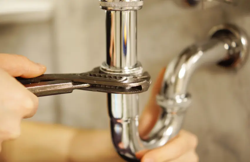 Plumber tightens a chrome pipe under a sink with a wrench on a P-trap.